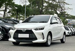 Toyota Agya GR Sport warna putih difoto dari sudut depan samping, menampilkan desain city car terbaru dengan grille depan trapesium tajam ala GR Sport, headlamp LED sipit modern, dan velg alloy hitam sporty. Sebagai armada ekonomis sewa mobil di Medan, Agya menjadi pilihan tepat untuk perjalanan dalam kota, solo traveler, pasangan, atau keluarga kecil yang mengutamakan efisiensi bahan bakar dan kemudahan parkir di area padat seperti pusat kota Medan.