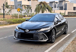 Toyota Camry warna silver difoto dari sudut depan samping, menampilkan desain sedan eksekutif dengan grille depan besar bergaya sporty, headlamp LED tajam, garis body yang mengalir elegan, dan velg alloy multi-spoke. Sebagai armada premium sewa mobil di Medan, Camry menjadi pilihan sedan mewah untuk kebutuhan protokoler, wedding car, jemputan tamu VIP/eksekutif perusahaan, hingga perjalanan bisnis yang mengutamakan kenyamanan dan kesan formal-elegan.