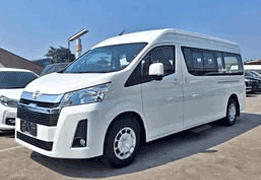 Toyota Hiace Premio warna silver difoto dari sudut depan samping, menampilkan desain generasi terbaru dengan bodi lebih besar dan lega dibanding Hiace Commuter, grille depan modern dengan aksen krom, serta kaca jendela lebar di sepanjang kabin. Sebagai armada premium sewa mobil di Medan, Hiace Premio cocok untuk rombongan yang menginginkan kenyamanan lebih tinggi, seperti VIP transport, perjalanan bisnis rombongan, wedding car, hingga city tour ke Danau Toba dan Berastagi dengan kapasitas hingga 13-14 penumpang.